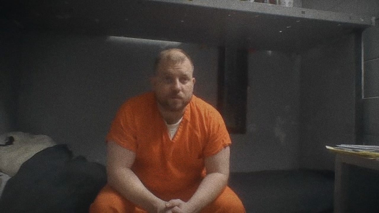 Ryan Nichols in an orange jumpsuit seated on a bunk during a video visit from the DC Jail