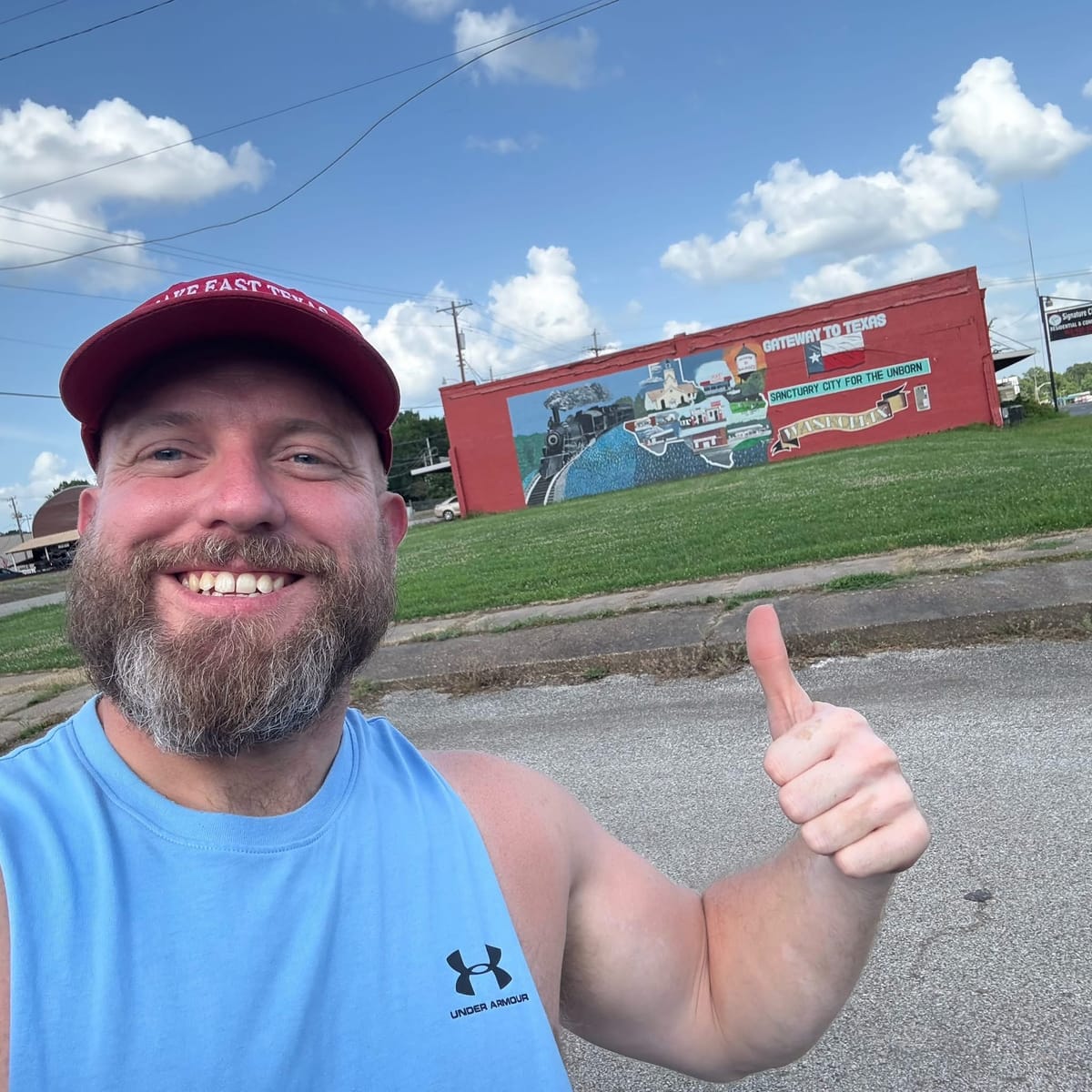Ryan Nichols today, smiling with a thumbs up in front of a red mural in East Texas