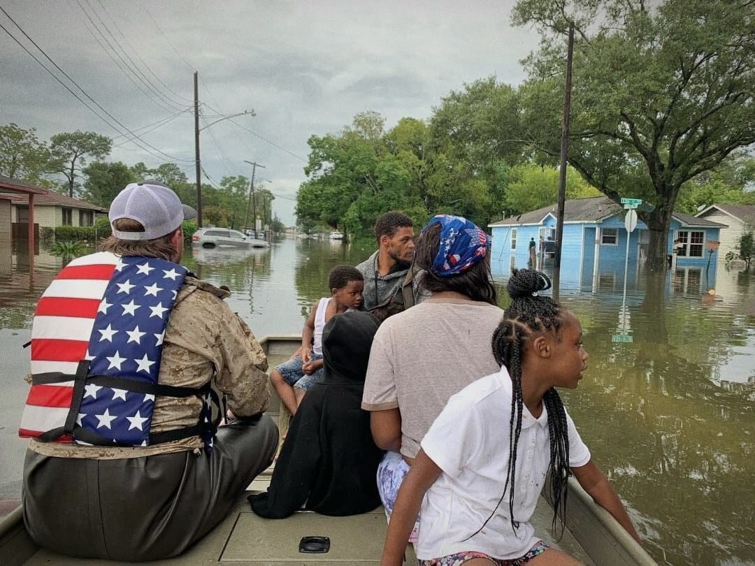A rescued family seated in the boat, life vests on, floodwater around them